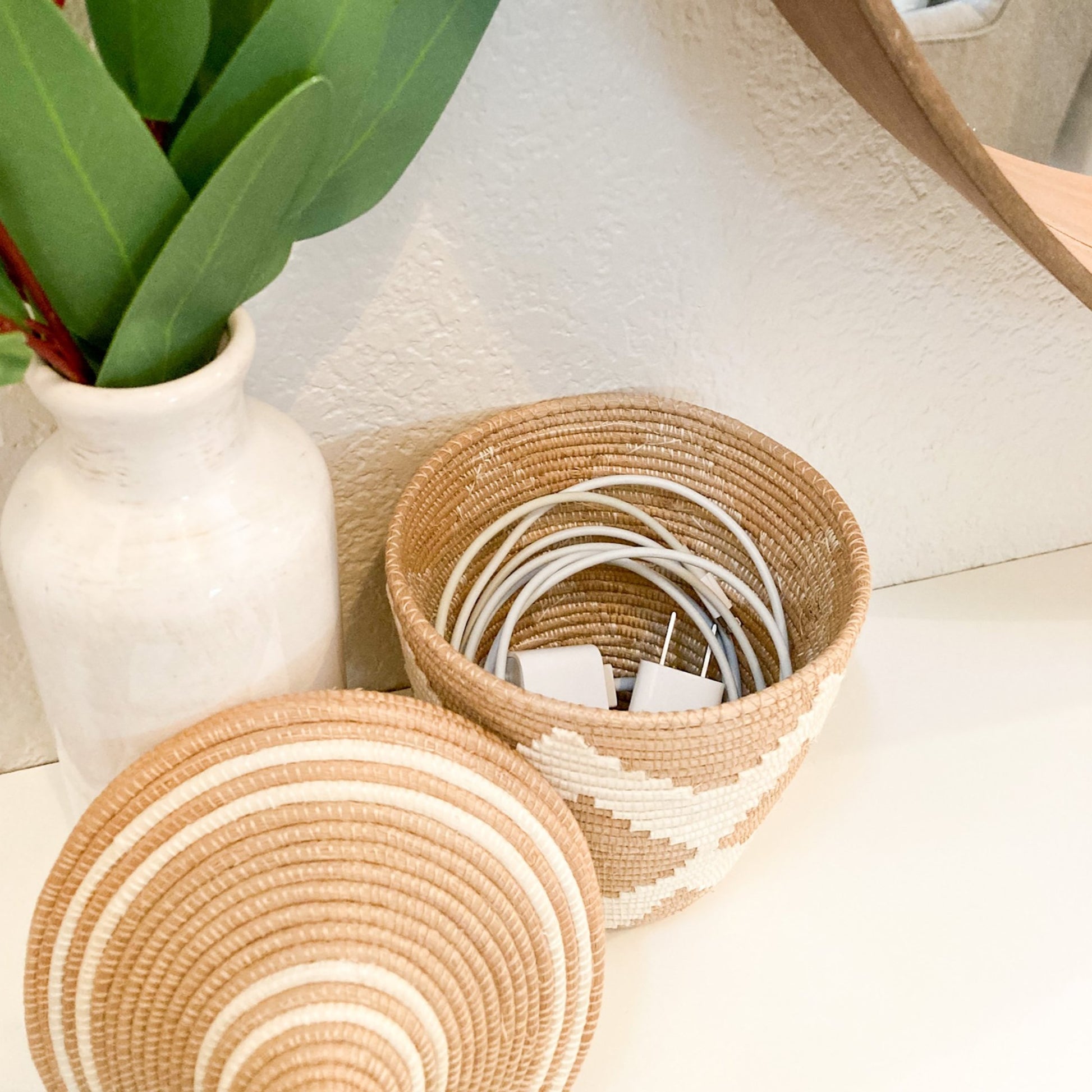 small woven basket with phone chargers inside.  The basket lid is propped up against the basket.  This basket is on an entryway table.