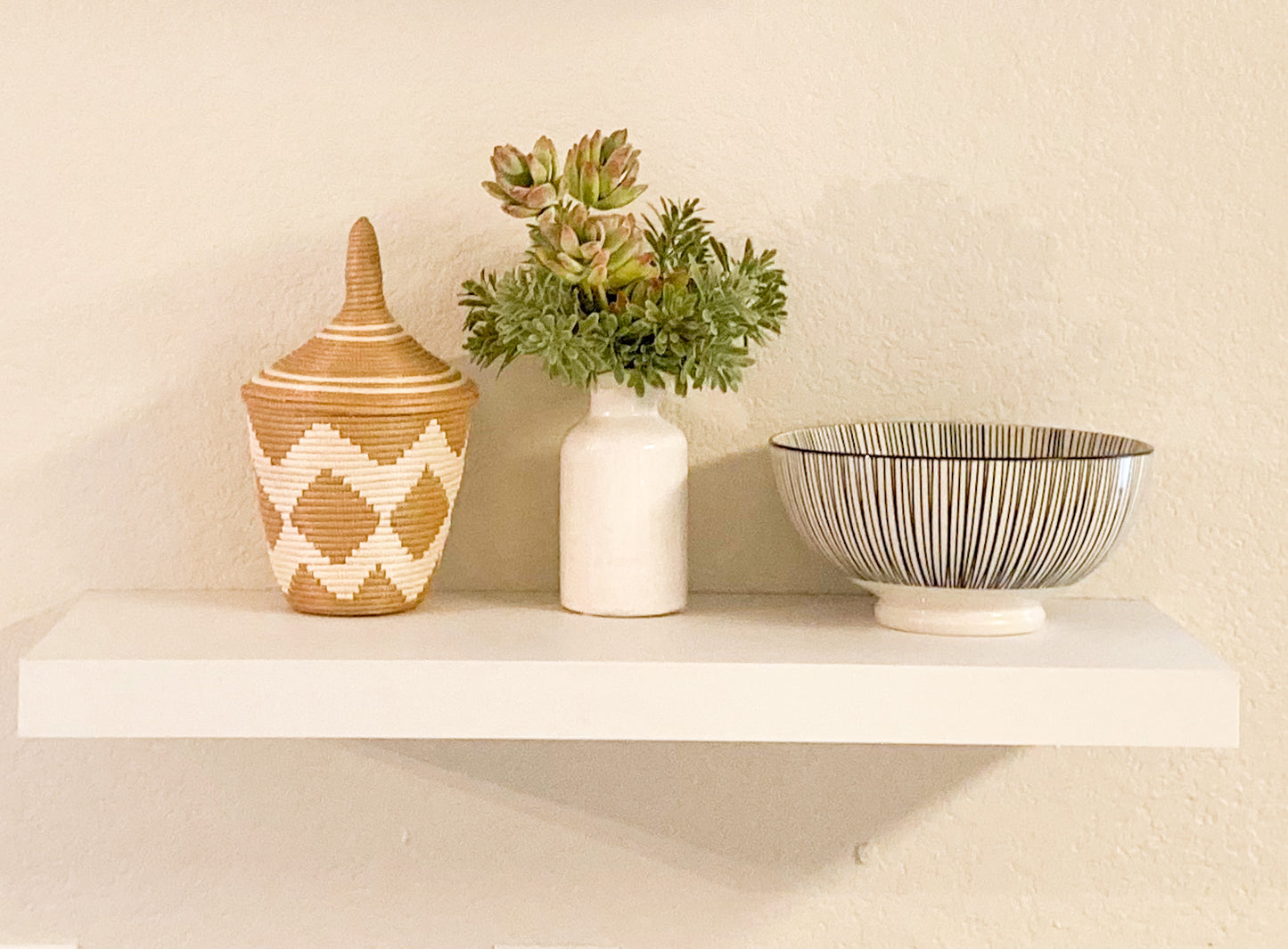 woven basket with white zig zag pattern and pointed lid, faux green succulent plant, and black and white striped bowl on shelf