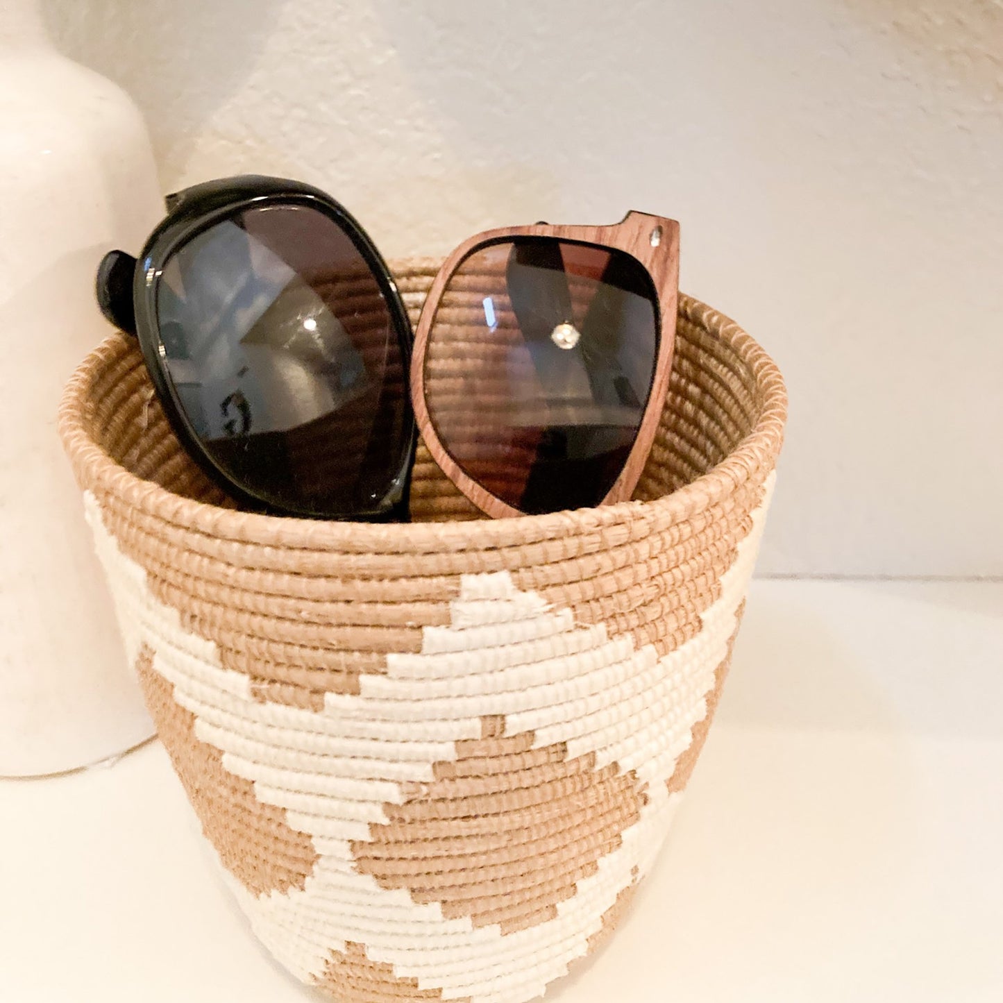 small woven basket with white zig zag pattern holding suglasses on entryway table