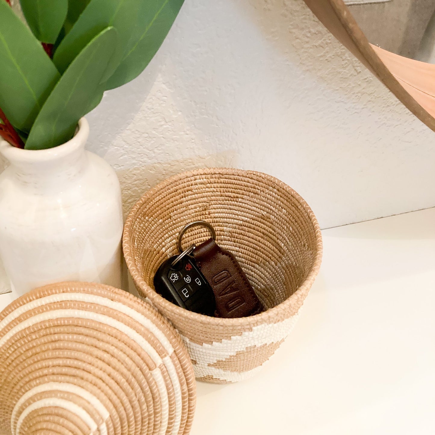 woven small basket with white zig zag pattern. Car keys are stored inside of basket and the lid is propped up against the basket.  The basket is on an entry way table.